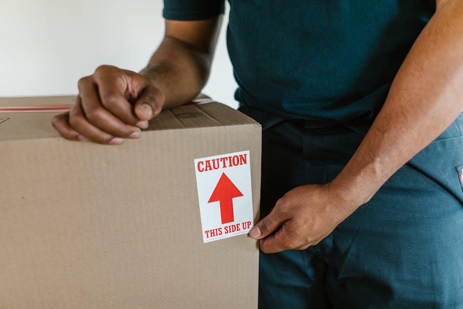 Inside a property, a professional moving company is in the process of packing and preparing household items for a home relocation in Kentish Town. Visible on the floor are several cardboard boxes, som
